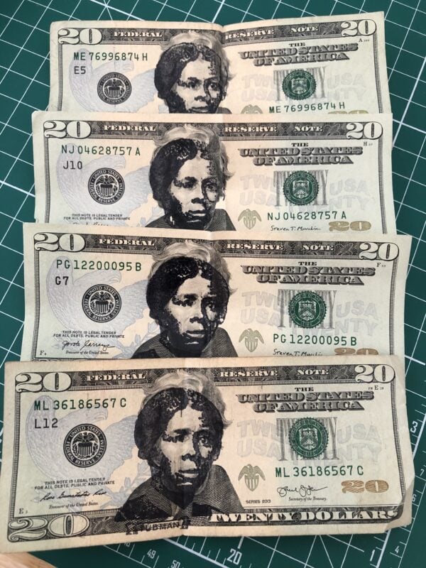 Four United States $20 bills with an image of Harriet Tubman stamped in black ink over Andrew Jackson's face